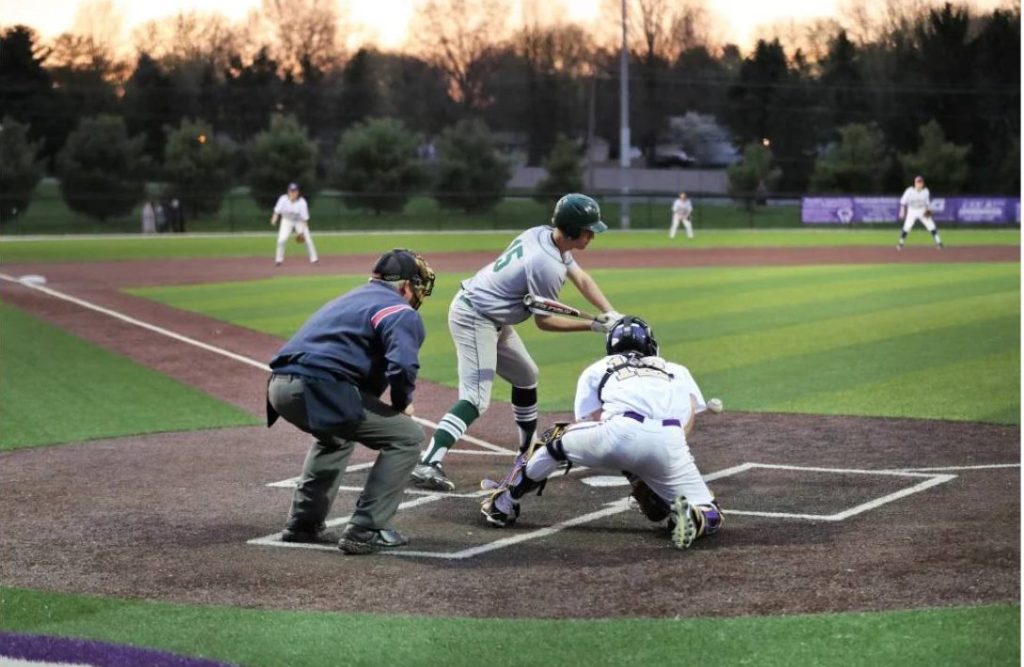 People play baseball in the foreground and a baseball diamond is in the background.